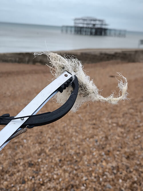 Beach clean up organized at BrightonSEO 2024 - a piece of plastic fishing net being held up with the view of the ocean and burned Brighton pier.